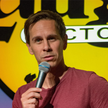 Comedian Jonesy holds a microphone while doing stand-up on a stage.